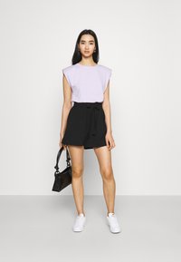 Top senza maniche lavanda con spalle strutturate, abbinato a pantaloni corti neri a vita alta e sneakers bianche. Accentato da una piccola borsa nera.