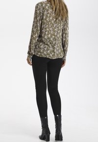 Langärmelige, olivgrüne Bluse mit kleinem Blumenmuster, kombiniert mit schwarzen engen Hosen und schwarzen Stiefeletten. Glatte Textur und lockere Passform.