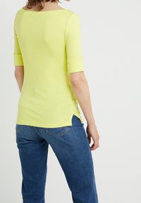 Ljust gul, figursydd topp med trekvartslånga ärmar, rundad halsringning och fickor i sidorna, matchad med blå jeans med bakfickor.