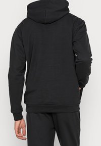 Svart hoodie med dragsko i huvan, långa ärmar och en avslappnad passform. Har ribbade mudd och nederkant, tillverkad av mjukt, slätt tyg.