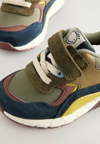 Buntes Sneaker-Modell aus olivgrünem, marineblauem und braunem Wildleder. Mit Klettverschluss, beigen Schnürsenkeln und gesprenkelter Sohle.