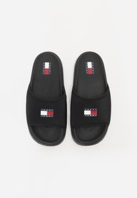 Černé klouzací sandály s měkkým, texturovaným svrškem. Obsahují logo na záplatě v modré, bílé a červené barvě. Plná podešev s hladkým povrchem.