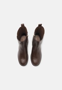 Stivali ankle in pelle marrone con una finitura liscia, zip laterali, punte tonde e linguette sul retro. Interno foderato per il comfort.