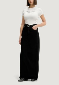 Bílá košile s krátkým rukávem a černým logem "Tommy Jeans", doplněná o dlouhou černou džínovou sukni s vysokým pasem a stříbrným opaskem.