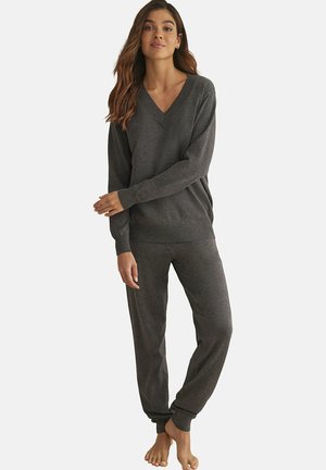 Grijze gebreide loungewear set met een V-hals trui met geribde manchetten en zoom, gecombineerd met bijpassende elastische broek. Zachte textuur.
