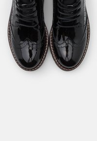 Black patent leather brogues with a wingtip design, featuring polished texture, round toe, and tonal laces sitting on a textured sole.
