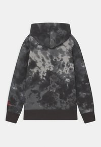 Sweatshirt à capuche avec un motif tie-dye, présentant des nuances de gris et de noir, avec une taille sombre et un détail de couture rouge sur la manche.