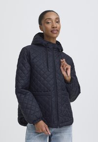 Pufasta mornarsko plava jakna s kapuljačom, prednjim zatvaračem na patent i elastičnim manšetama. Ima dva bočna džepa. Lagani, pufasti dizajn s glatkom završnom obradom.