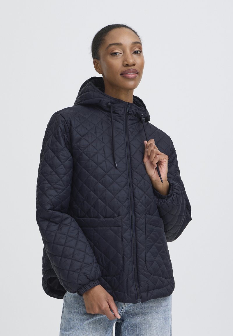 Pufasta mornarsko plava jakna s kapuljačom, prednjim zatvaračem na patent i elastičnim manšetama. Ima dva bočna džepa. Lagani, pufasti dizajn s glatkom završnom obradom.