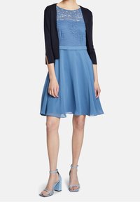 Blå klänning med spetskorsett, lager av kjol och en marinblå kofta. Har en figursydd midja och A-linjeform. Matchas med ljusblå klackar.