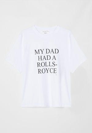 Bílý tričko s krátkým rukávem vyrobené z bavlny. Vyznačuje se tučným černým textem: "MŮJ TÁTA MĚL ROLLS-ROYCE." Logo štítku na límci. Jednoduchý design.