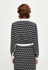 Black and white patterned dress featuring long sleeves, a white collar, and a waist belt. The fabric has a geometric diamond design.