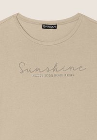 Camiseta de manga corta beige en una tela suave con un eslogan texturizado adornado con piedras de strass: "La luz del sol hace brillar tu alma". Cuello redondo.