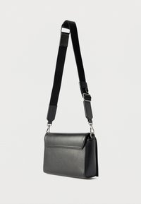 Μαύρη ορθογώνια δερμάτινη τσάντα χιαστί με ρυθμιζόμενο φαρδύ λουράκι και ασημένια μεταλλικά κούμπωμα, σε απλό φωτεινό φόντο.