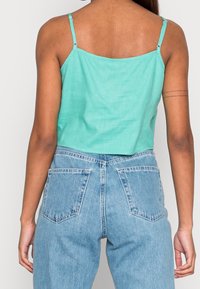 Türkisfarbenes Crop-Top mit dünnen Trägern und weitem Schnitt, kombiniert mit hellblauen, hoch taillierten Jeans mit Gesäßtaschen.