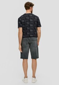 T-shirt noir avec un motif de texte répétitif, associé à un short en denim gris foncé. Texture lisse et coupe décontractée, porté avec des baskets blanches.