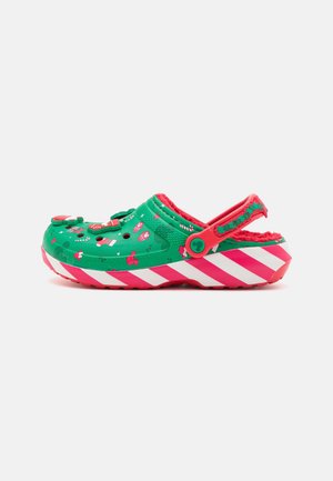 Zapato estilo crocs verde con acentos rojos. Presenta patrones festivos y una suela a rayas en rosa y blanco. Incluye una correa en la parte trasera para un ajuste seguro.