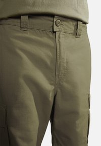 Shorts cargo en vert olive, fabriqués en tissu léger. Dotés d'une fermeture à bouton à l'avant, de poches latérales et d'une texture subtile.
