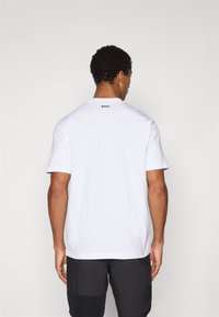 T-shirt blanc à manches courtes avec un col rond, arborant un logo noir "BOSS" au dos. Tissu doux, coupe standard, design minimaliste.