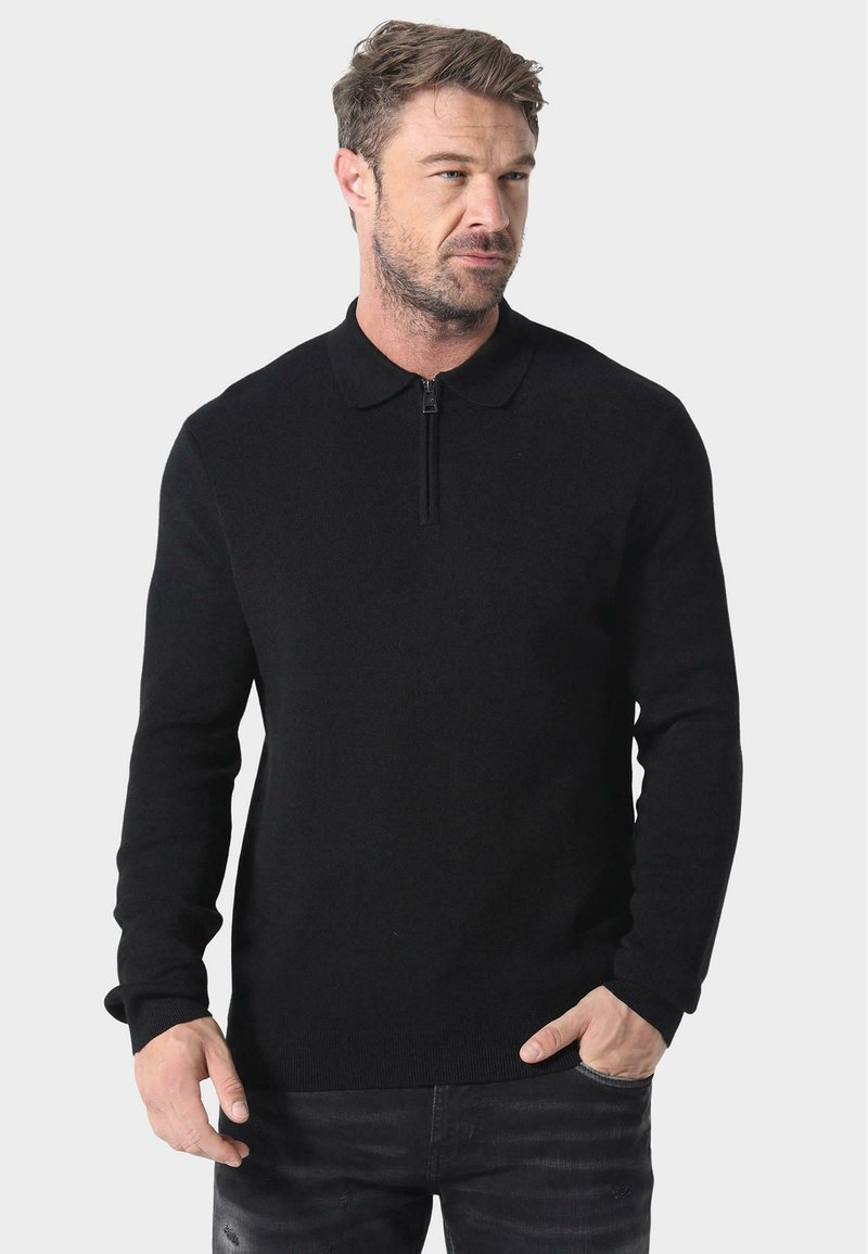 Svart strikket genser med glidelås i kragen, lange ermer og tettsittende design. Stoffet ser mykt ut med en jevn tekstur.