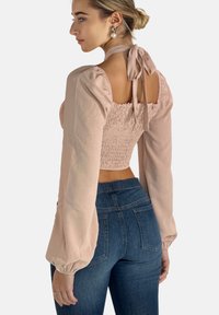Top corto rosa con mangas abullonadas y fruncido, con la espalda descubierta y cierre de lazo. Combinado con jeans de mezclilla oscuros de tiro alto, que cuentan con bolsillos traseros.