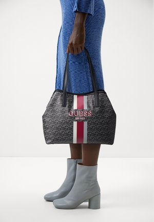 Czarna torba na ramię w wzory z czerwonymi i białymi paskami, z wyraźnym logo "GUESS". Połączona z jasnoniebieskimi botkami za kostkę.