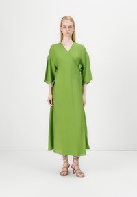 Lang, grønn omslagskjole med korte kimonoermer og et strukturert stoff. Har sidelommer og en flytende silhuett. Minimalistisk design.