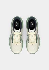 Des chaussures de course légères avec un upper crème, des accents verts, un matériau en maille et des motifs texturés sur la surface.