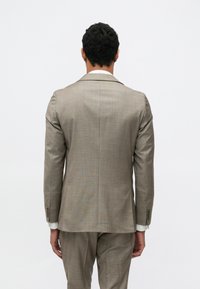 Giacca da abito color marrone chiaro con motivo a trama, spacco singolo e rever a lancia. Vestibilità sartoriale con polsini a quattro bottoni e fodera interna a contrasto.