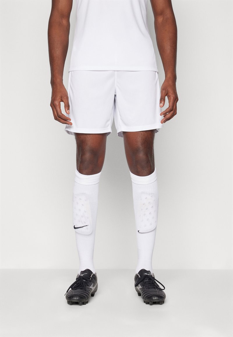 Hvide athletic shorts og en matchende skjorte, parret med sorte fodboldstøvler og knælange hvide sokker med et sort logo.