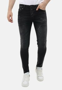 Zwarte skinny jeans met versleten details en een vervaagde textuur. Heeft een klassiek vijf-pocket ontwerp en afgesleten plekken op de knieën.