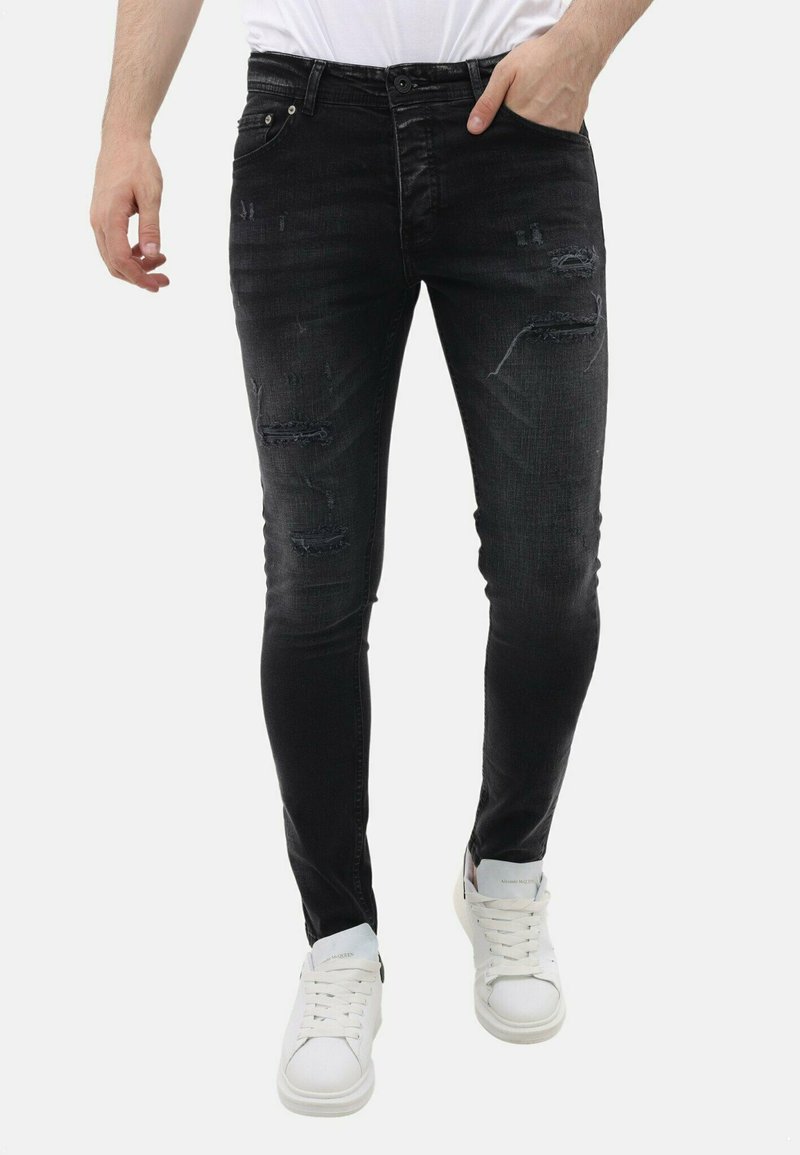 Zwarte skinny jeans met versleten details en een vervaagde textuur. Heeft een klassiek vijf-pocket ontwerp en afgesleten plekken op de knieën.