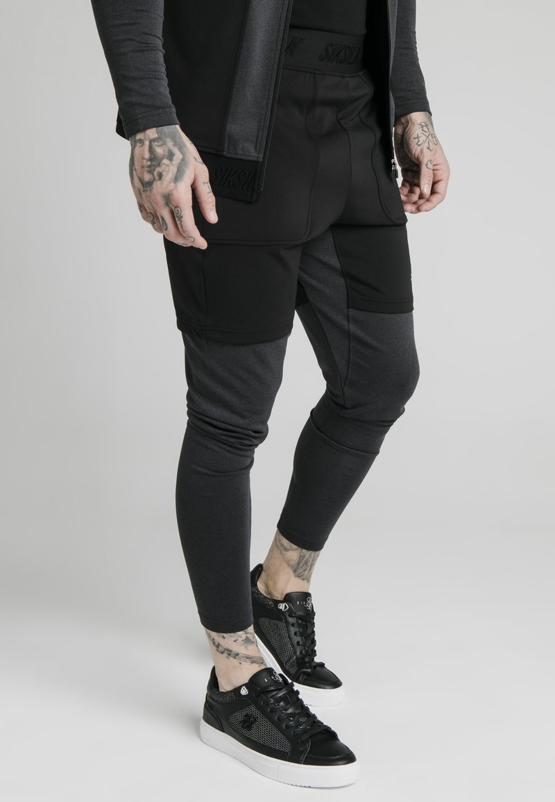 Black and gray athletic outfit featuring tapered pants and a fitted top, both in contrasting textures; worn with black sneakers.