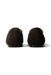 Paire de chaussures plates en suède marron foncé vues de dos sur une surface blanche avec des semelles basses noires et une couture minimaliste.