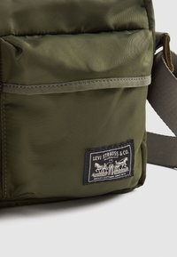 Borsa in tessuto verde oliva di Levi Strauss & Co. con tasca frontale e patch logo rettangolare nero che mostra due cavalli e testo.