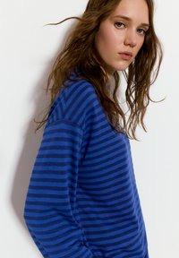 Modrý a námořnický pruhovaný top s dlouhým rukávem vyrobený z měkké látky, nabízející volný střih a široké rukávy, s kulatým výstřihem.