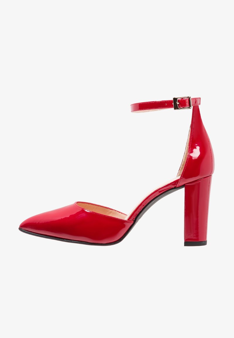 Chaussure à talon haut en cuir verni rouge avec bout pointu et bride à la cheville avec boucle, vue de côté sur fond blanc.