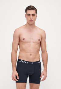 Fekete boxeralsó, kontrasztos fehér "JORDAN" logóval ellátott derékkal, testhez simuló kialakítással és sima pamut textúrával. A modellen nincs felső.