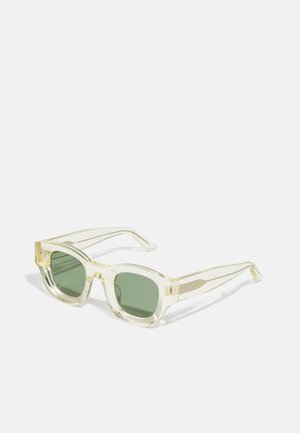 Lunettes de soleil claires et surdimensionnées avec des verres verts, en forme rectangulaire, avec des branches texturées et une monture transparente. Des accents comprennent un motif subtil.