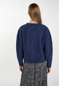 Granatowy sweter dzianinowy z teksturowanym wzorem w diamenty, z okrągłym dekoltem i ściągaczem u dołu. Połączony z wzorzystą spódnicą.