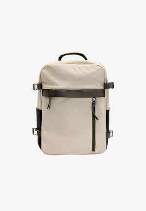 Beżowy plecak o prostokątnym kształcie, z dwoma czarnymi akcentami po bokach, przednią kieszenią na zamek oraz metalowymi elementami na paskach. Gładka faktura.