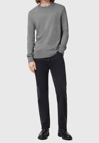 Grauer langärmeliger Pullover aus leichtem Material, mit Rundhalsausschnitt und dezenter Textur, kombiniert mit schwarzen gerade geschnittenen Jeans und schwarzen Stiefeln.