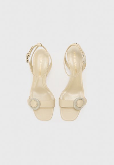 Beige højhælede sandaler med en bred rem og en cirkulær detalje. Lavet af glat læder med et elegant, minimalistisk design.