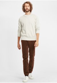 Light grey sweatshirt with ribbed cuffs and hem, paired with brown corduroy pants. Model wears white sneakers. Simple, relaxed design.