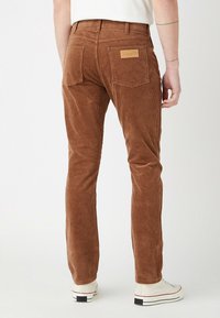 Pantalon en velours côtelé marron avec une finition texturée, doté d'un patch en cuir sur la ceinture arrière, cinq poches et une coupe slim.