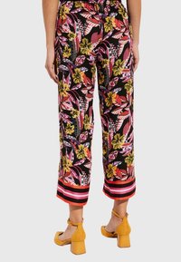 Pantalon en tissu léger avec un imprimé floral audacieux en rouge, jaune et rose sur fond noir. Avec un ourlet rayé.