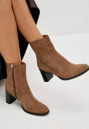 Bottines en suède marron avec un talon carré, dotées d'une fermeture éclair sur le côté, d'une texture lisse et d'une silhouette épurée, idéales pour une tenue décontractée.