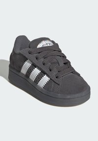 Black suede sneaker with black laces, white zigzag three stripes on the side, textured sole, and iridescent logo on the tongue.