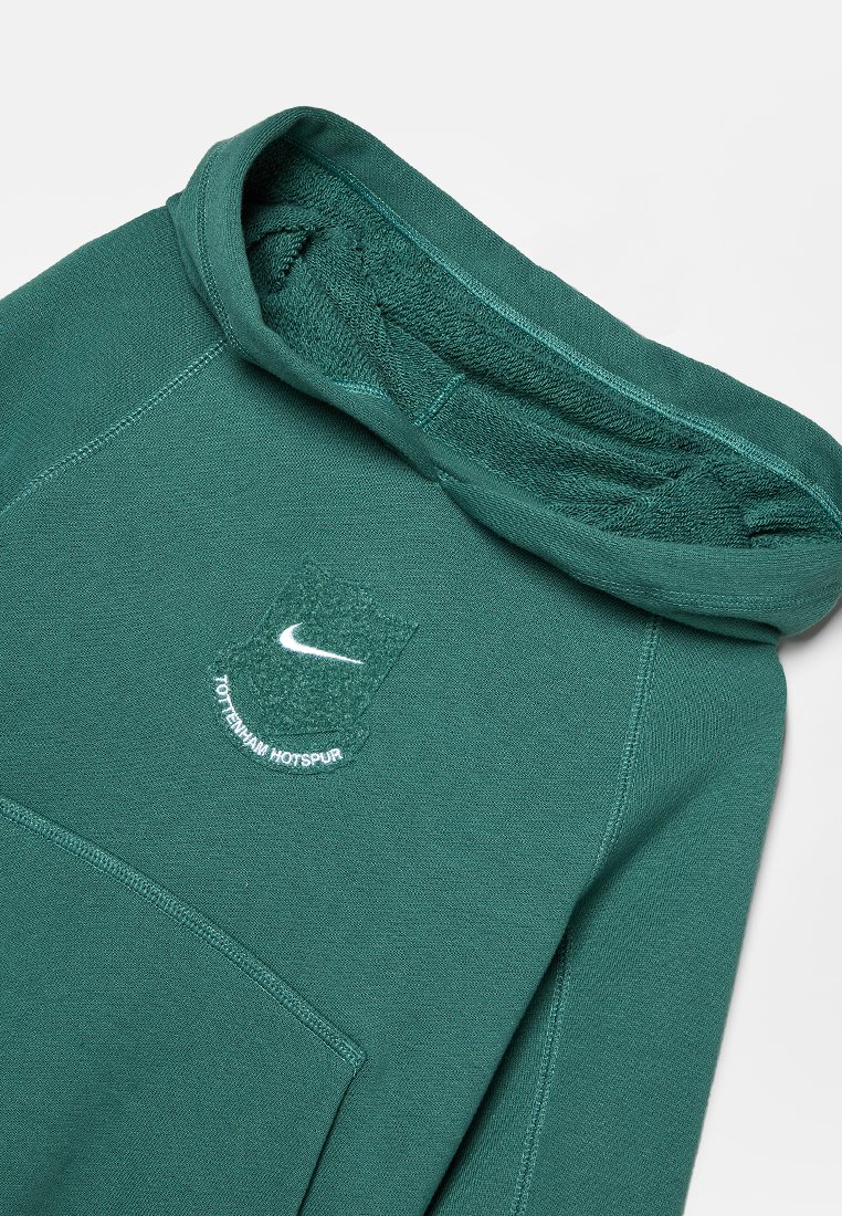 Haut à capuche vert foncé avec le logo Nike et le texte "Tottenham Hotspur" sur la poitrine, doté d'une poche kangourou à l'avant et de coutures visibles.
