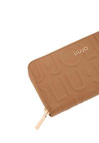 Portafoglio in pelle marrone con motivo a logo impresso, ferramenta color oro e chiusura con cerniera con tirante. Dettaglio della superficie testurizzata.